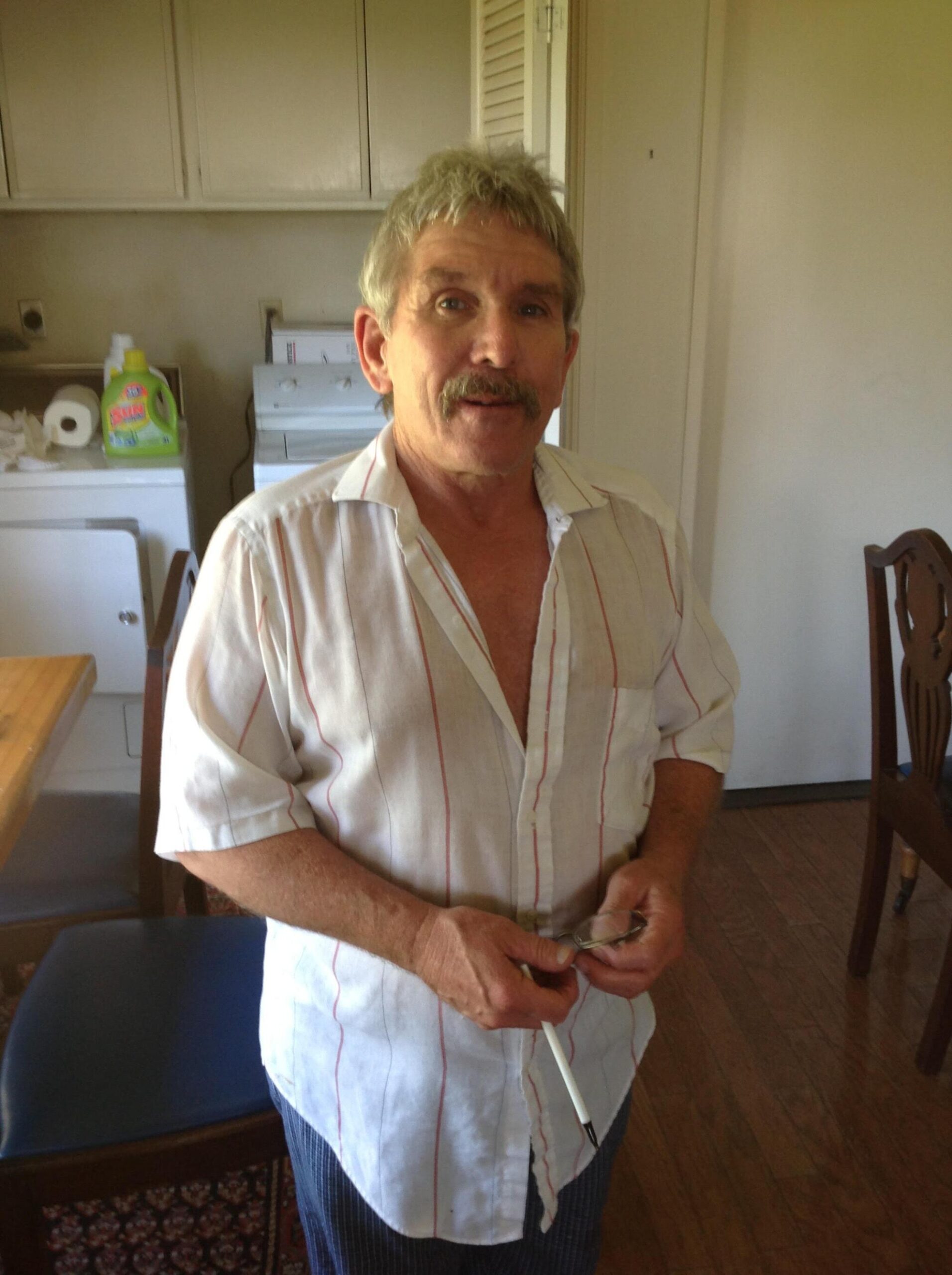 2018 photo of Andrew Daulton Lee with gray hair and in a white shirt standing in a room.