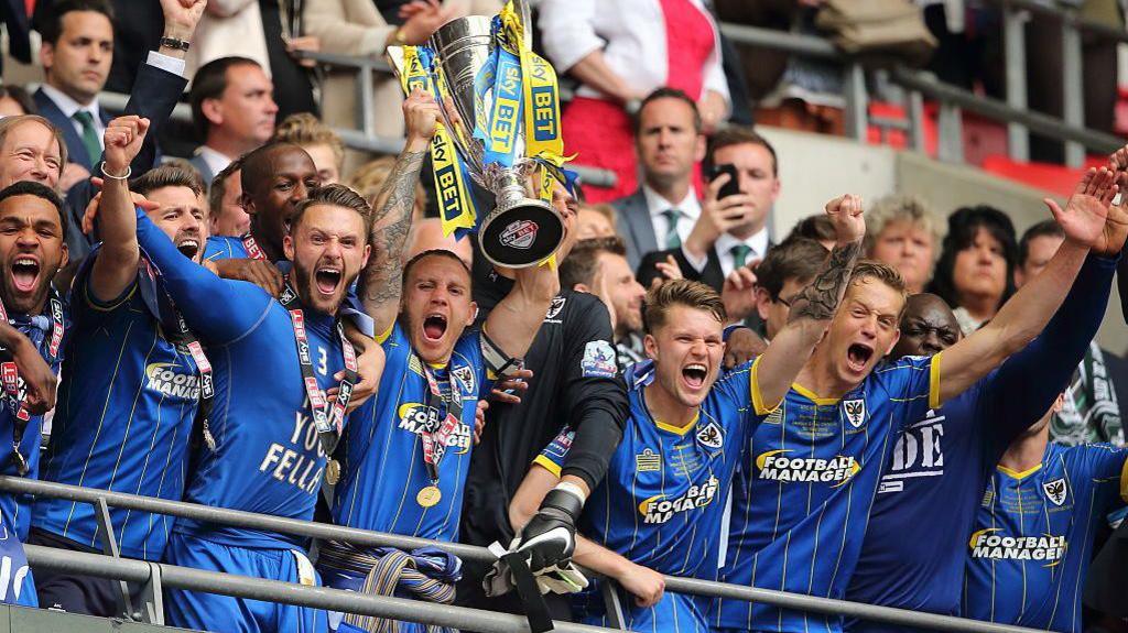 AFC Wimbledon's players celebrate with the League Two play-off final trophy