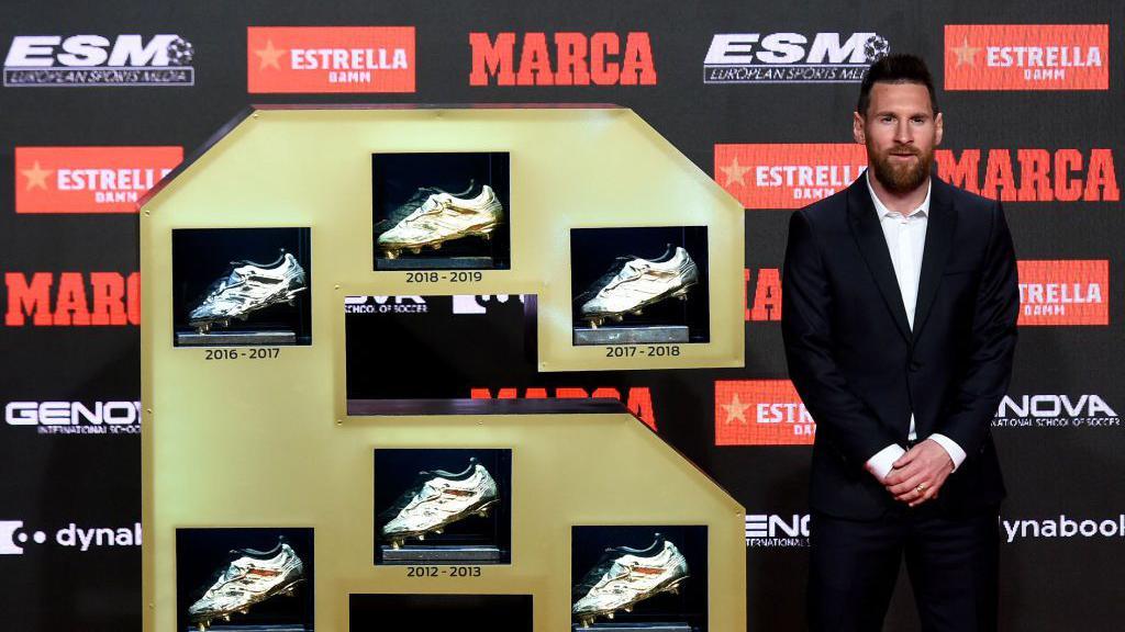 Lionel Messi standing next to his six Golden Shoes