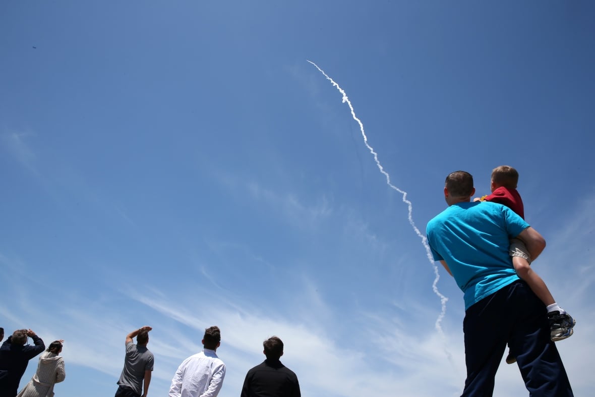 People look skyward at the trail left by a distant missile.