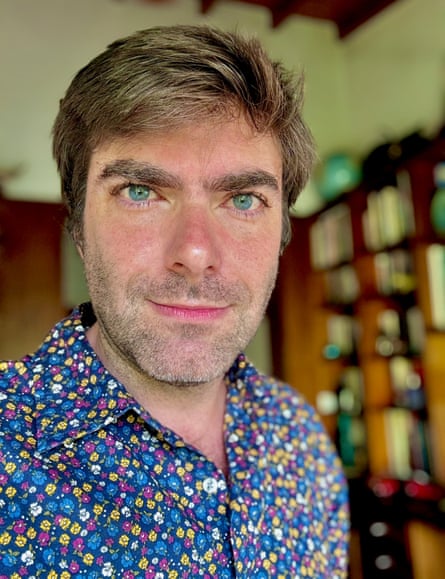 a man in a brightly colored floral shirt poses for a photo in front of a bookcase