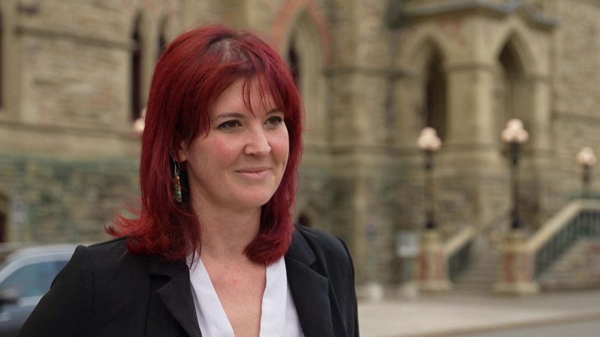 A woman with red hair standing in front of Parliament.
