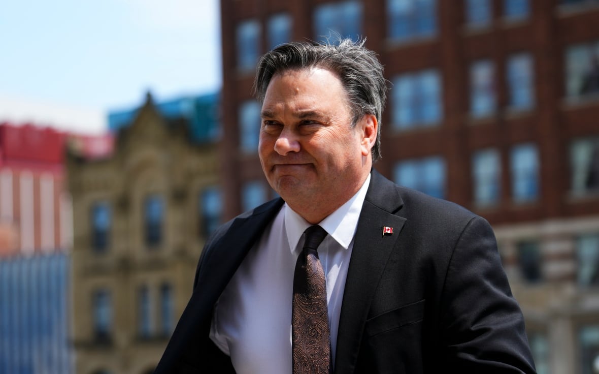 A man in a suit walks outside on a sunny day.