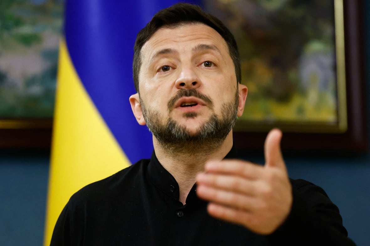 A man speaks in front of a yellow and blue flag.