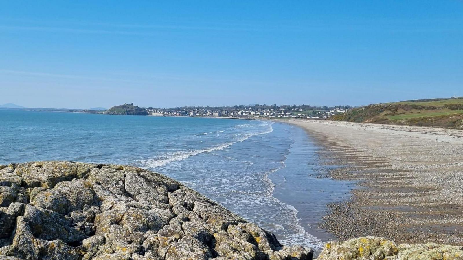 photograph of a rock and beach looking out towards the town of Cricceith with the castle just visible on the rock in the distance.  Blue skies above.