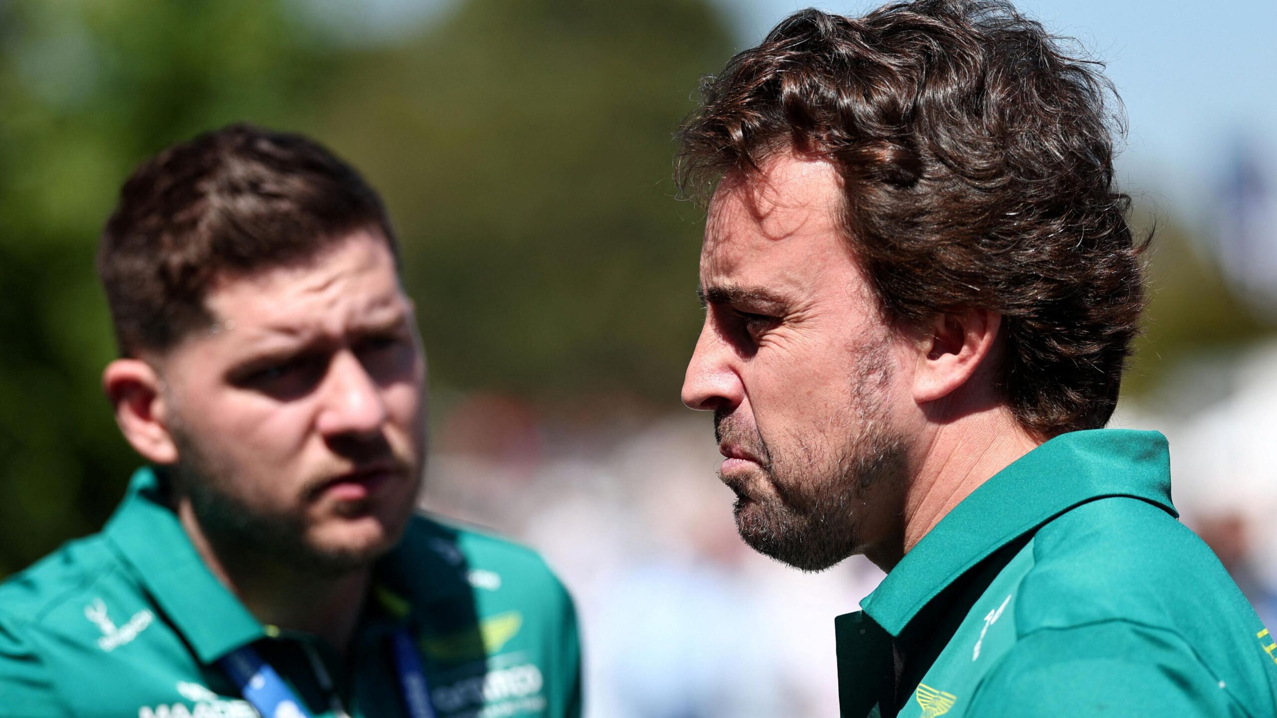 An Aston Martin team member speaks to Fernando Alonso, who is looking stern after not being able to drive in first practice for the Australian Grand Prix