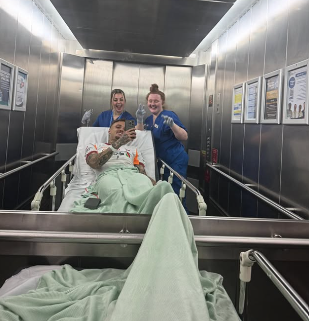 Noa Lang smiling from a hospital bed with two nurses at Whiston Hospital