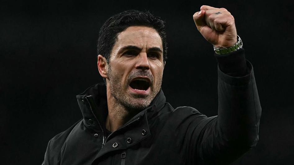 Arsenal manager Mikel Arteta, wearing a black coat, gives a clenched-fist celebration