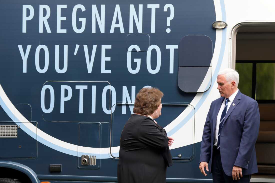 Former VP Mike Pence and Alexa Newman stand next to an RV that has an enormous sign that says, "Pregnant? You've got options."